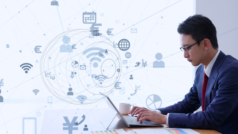 パソコンをしているスーツの男性の背後に、デジタル映像がレコメンドされている