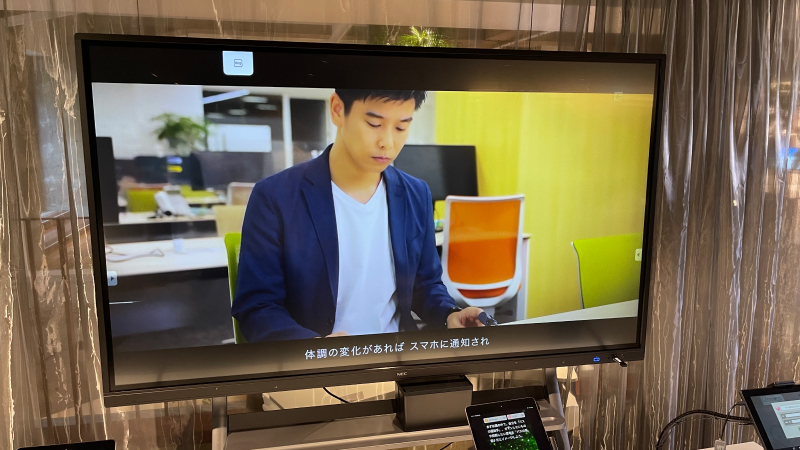 大型モニターにヘルスケアアプリを体験している男性が写っている